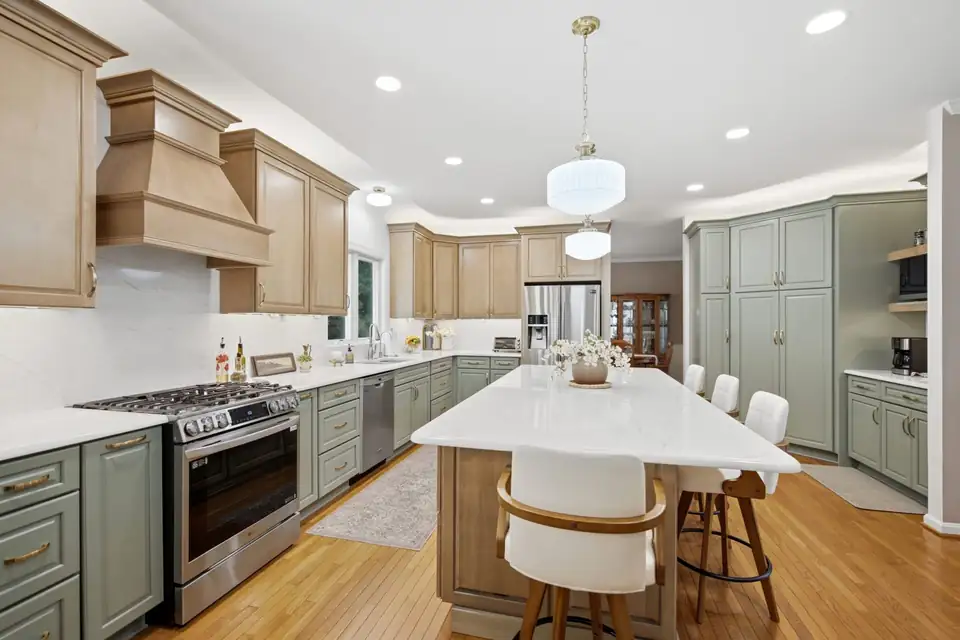 Kitchen remodeling Martinsburg WV: Petrasek family kitchen with Muted Moss green base cabinets, Wicker-finish wood uppers and island, Tyrol quartz counters and a chimney range hood