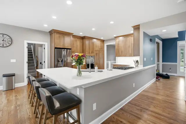 Harpers Ferry, WV open-plan kitchen with long quartz peninsula, gray base, wood cabinets and black counter stools