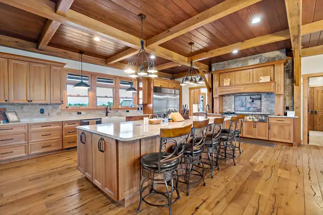 Kitchen by Mountaineer Kitchens & Baths with stained wood cabinets, a timber beam ceiling, a long island with seating and wide plank floors