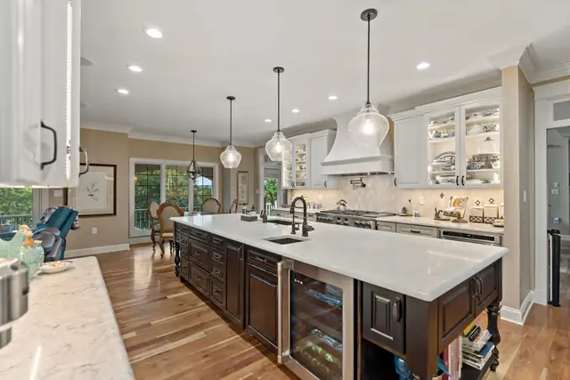 Open kitchen with gray and white cabinets, wood-topped island with stools and a linear pendant light