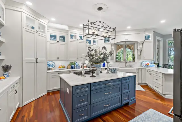 White kitchen with a navy blue island, an iron chandelier and cherry wood floors
